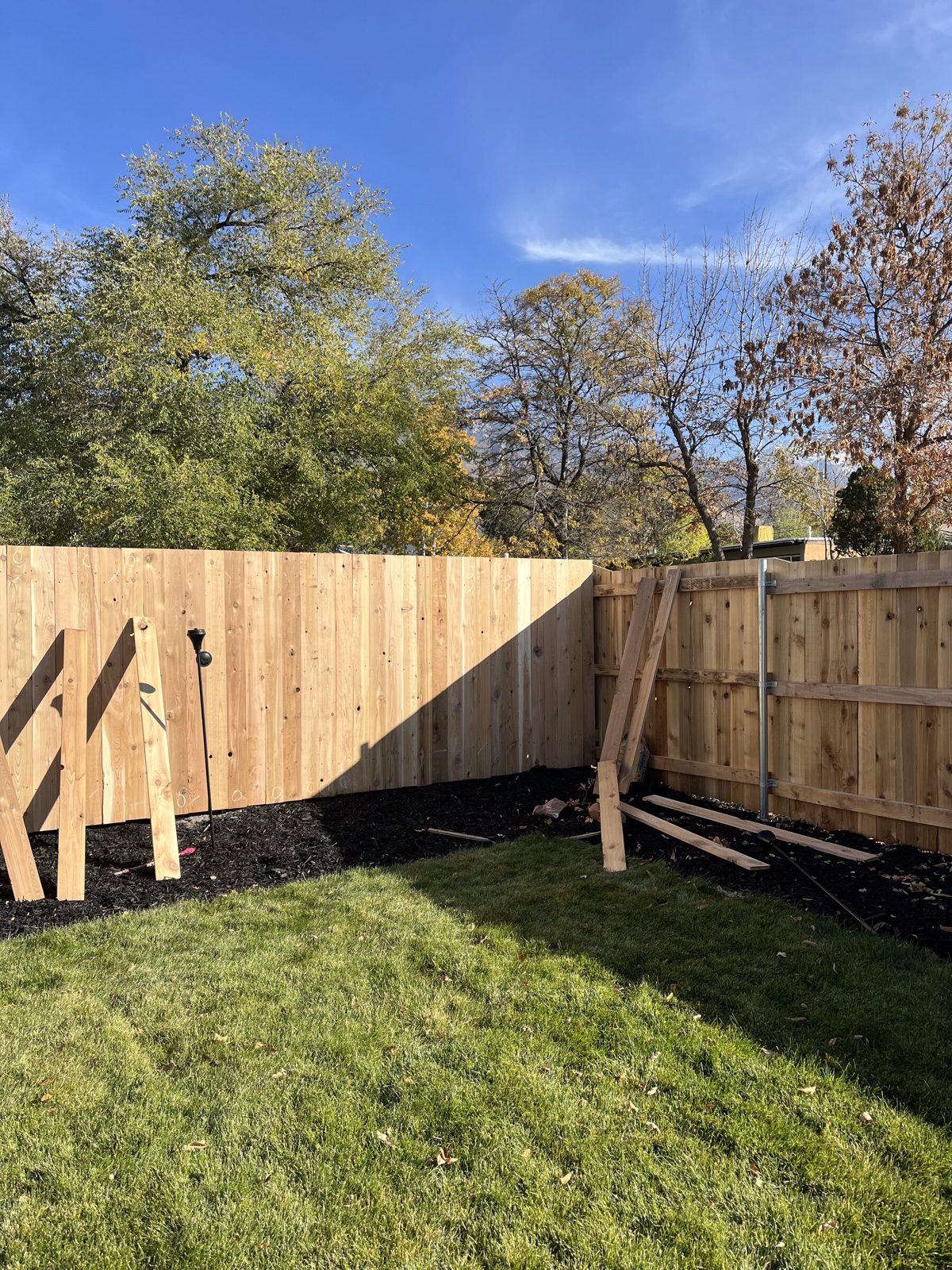Cedar privacy fence going up along a mulch bed under mature trees in the Salt Lake Valley