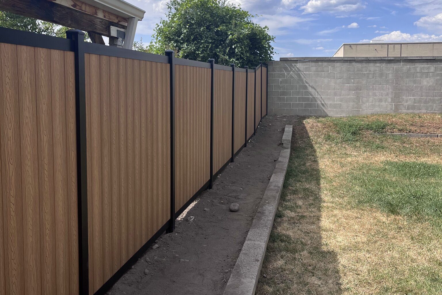 Light brown vertical composite privacy fence with black aluminum posts along a side yard, on a Trusted Fence job in Draper, UT