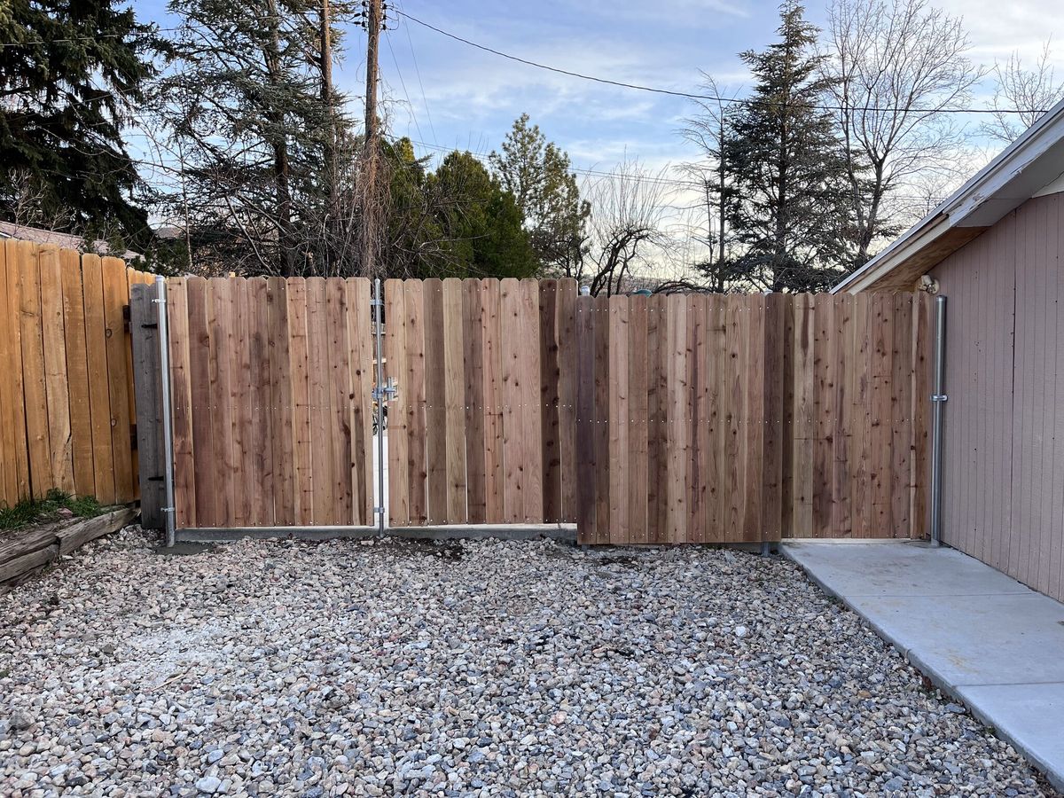 Cedar privacy fence with a double drive gate in metal frames across a gravel driveway in Bountiful, UT