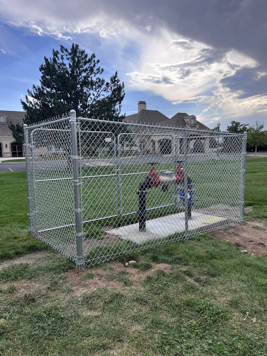 Galvanized chain link enclosure with a gate on a concrete pad in a grass lawn in the Salt Lake Valley
