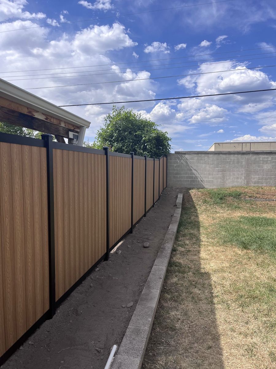 Woodgrain composite privacy fence with black posts beside a block wall in Draper, UT