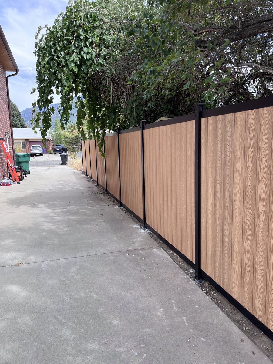 Woodgrain composite privacy fence with black posts along a concrete walkway in the Salt Lake Valley
