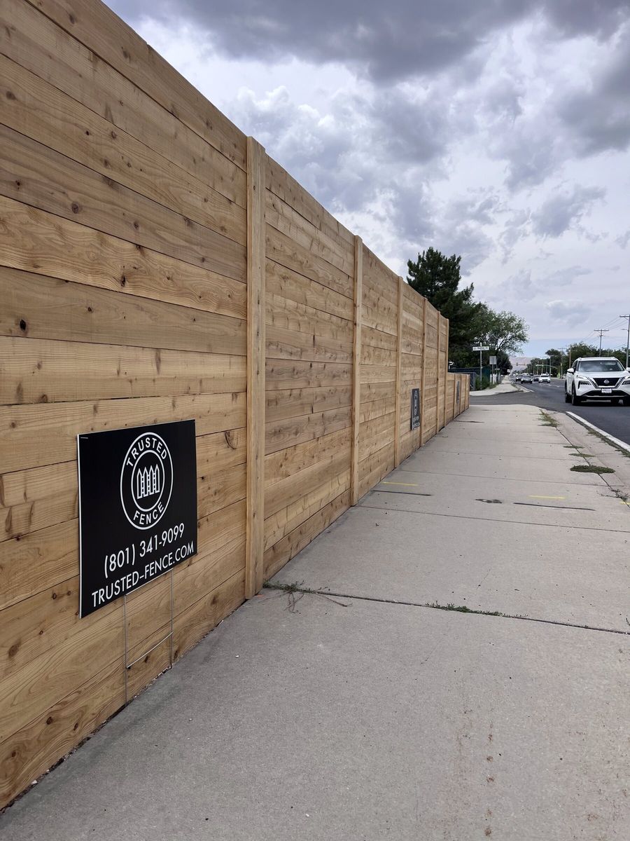 Tall horizontal wood fence with a Trusted Fence sign along a sidewalk in the Salt Lake Valley